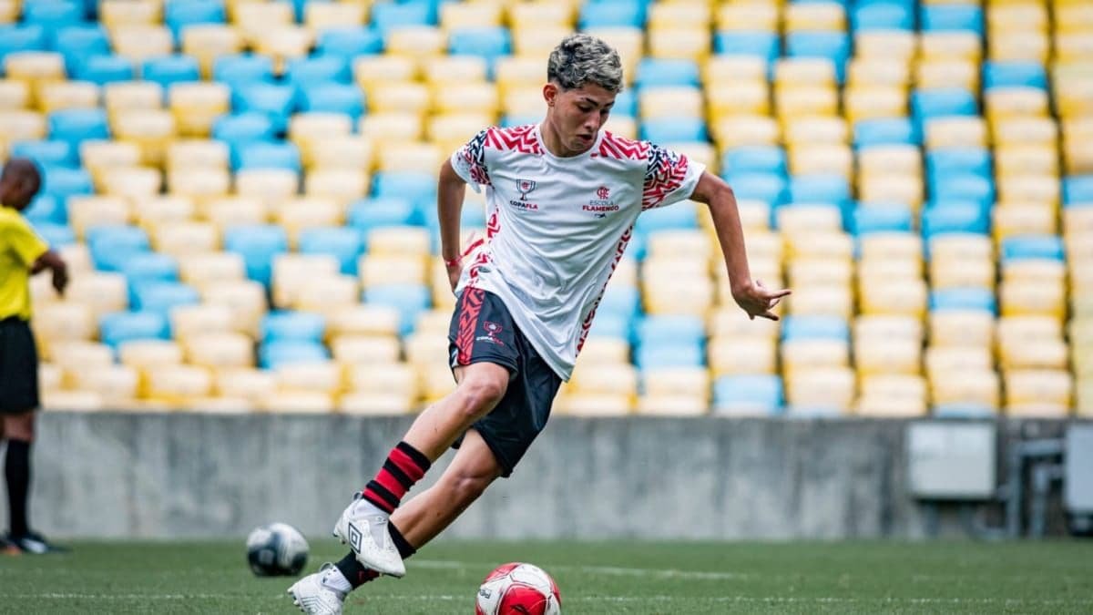 Jovem jogador com camisa da Escola Flamengo e da Copa Fla conduz a bola no gramado do Maracanã, com arquibancadas coloridas ao fundo