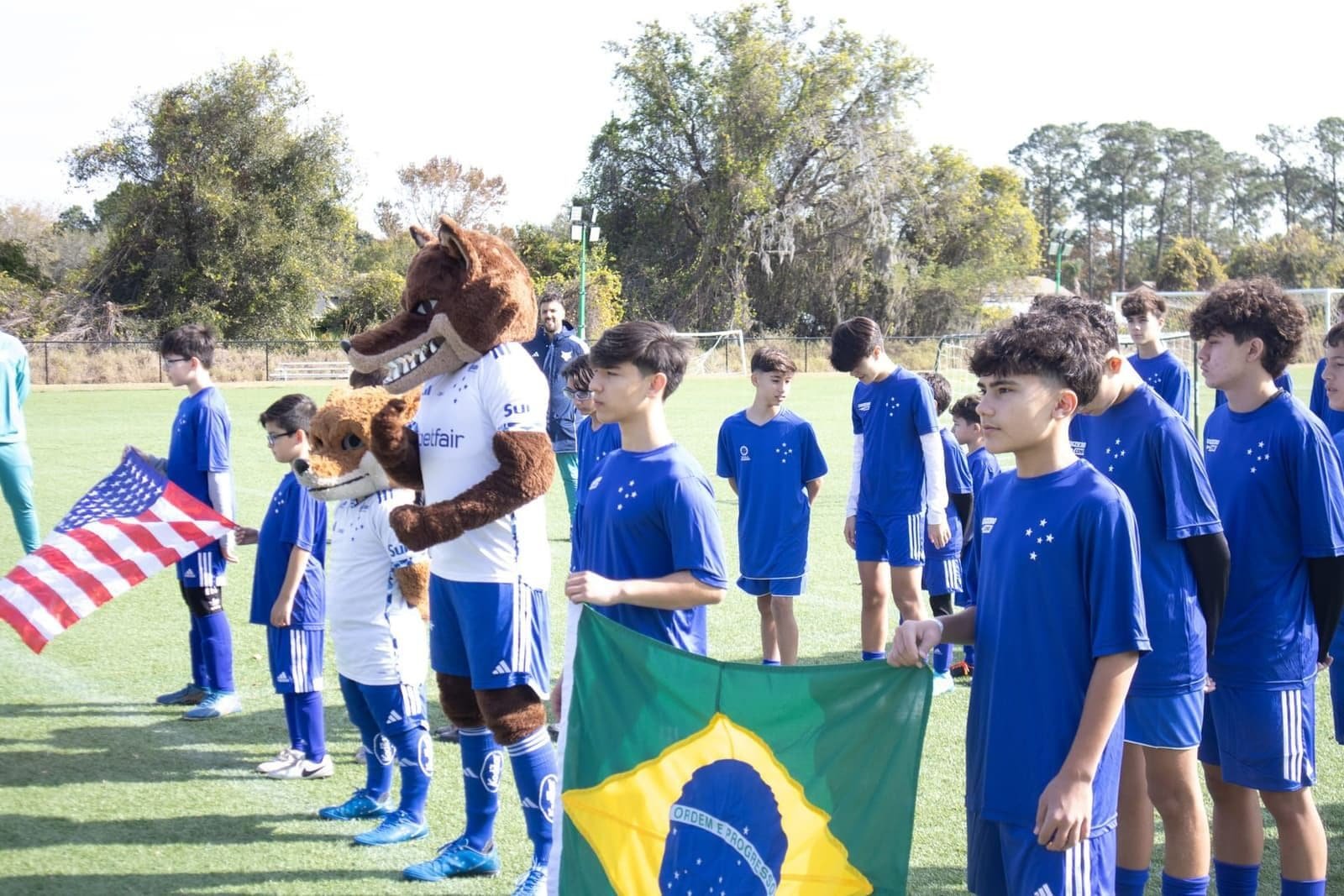 Cruzeiro Camp players lined up with the Brazilian and US flags alongside the club mascot
